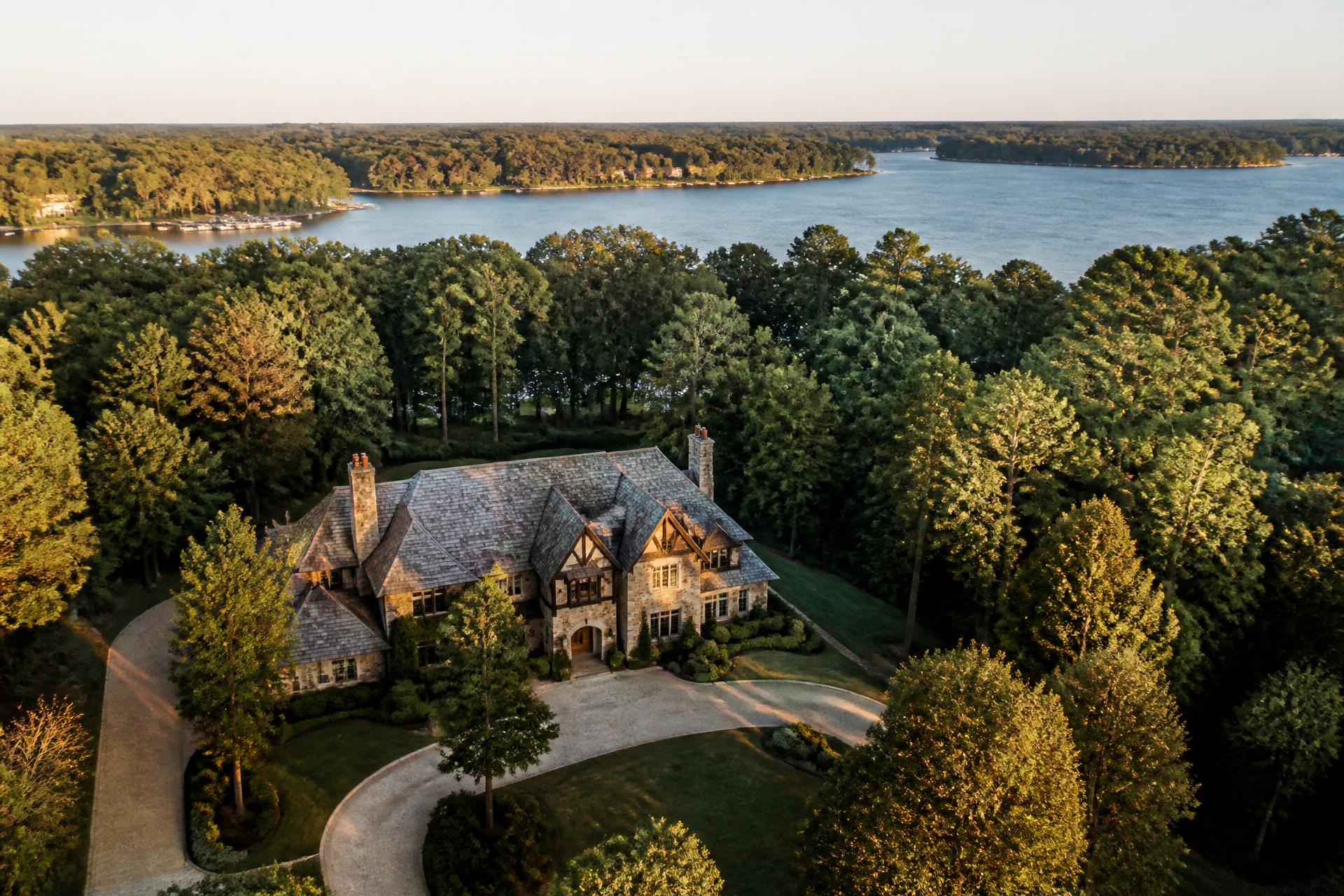 Aerial view of a stone-and-slate estate home at The Sanctuary set in hardwood forest above the Lake Wylie shoreline at golden hour