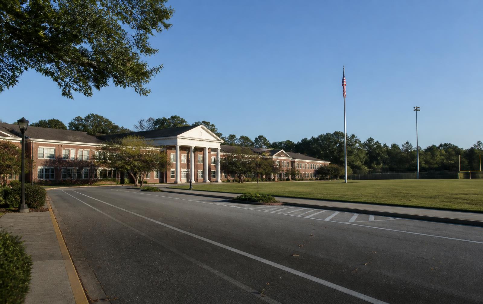 Brick school campus with white columns, flagpole, and athletic field near Lake Wylie